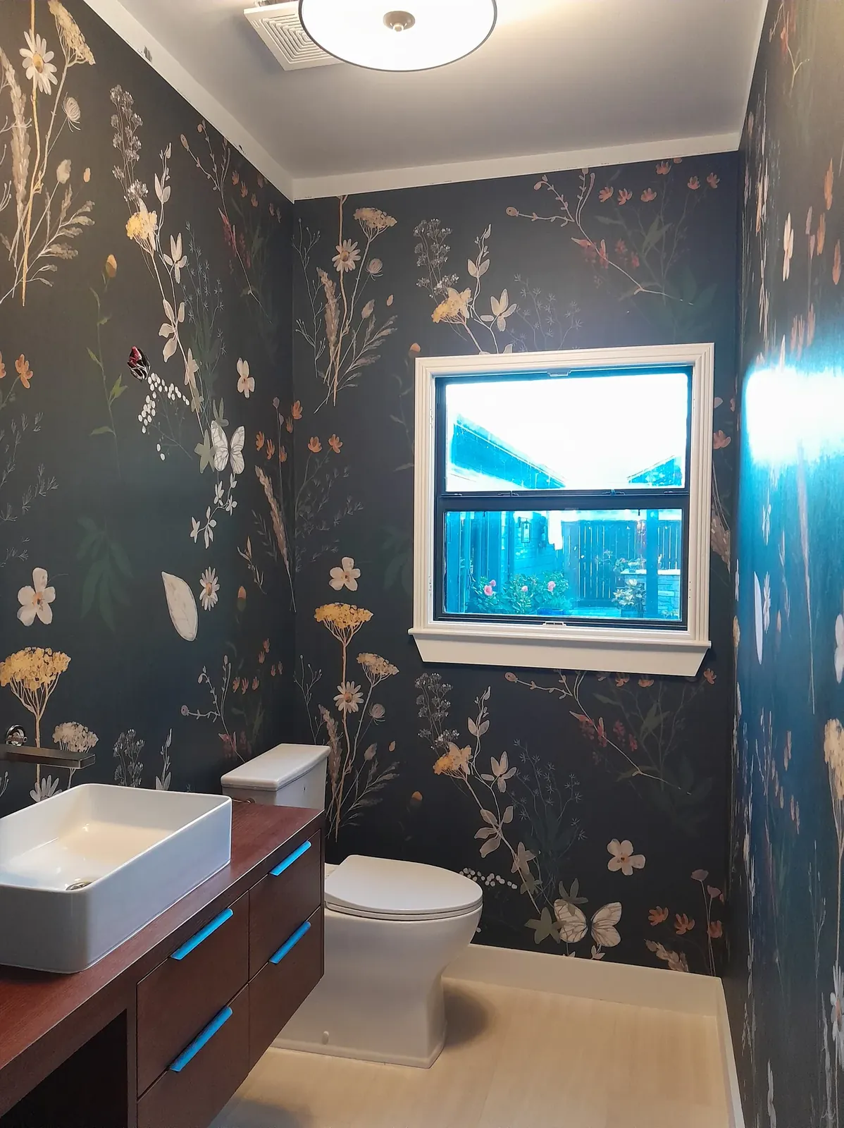 Powder room papered in a dark floral wallpaper, with a vessel sink and a window